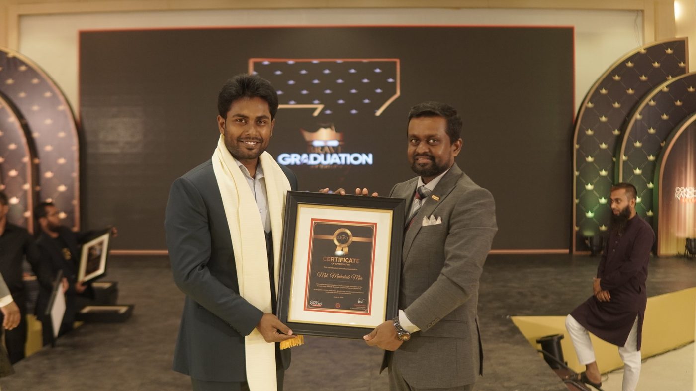 Md. Mahabub Mia holding a framed certificate on stage at the BRAVE graduation event, beside a presenter